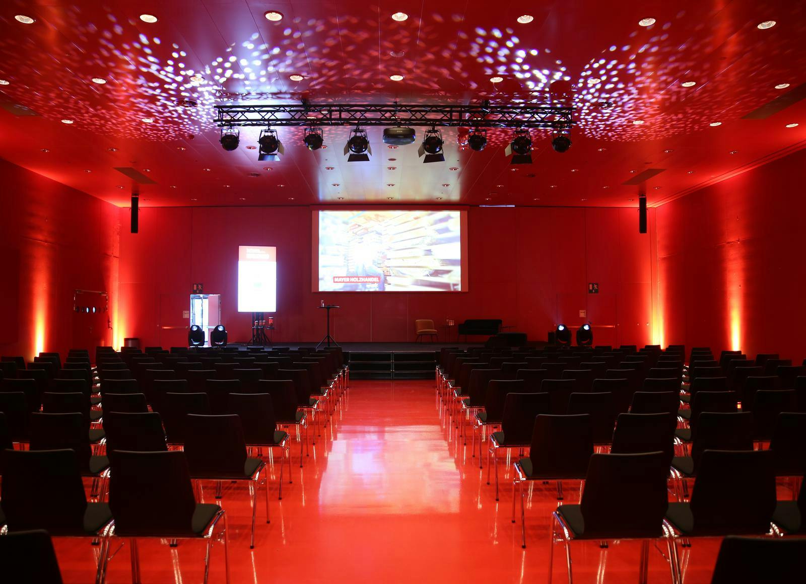Beleuchtete rote Halle mit Bestuhlung und Bühne. © 